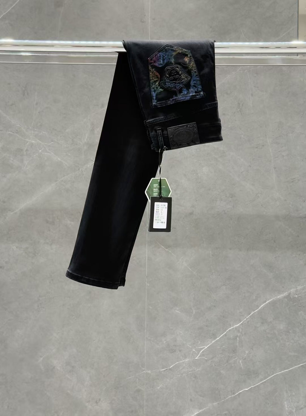 Dark denim jeans with a folded hem and colorful graphic patch on the back pocket area.
