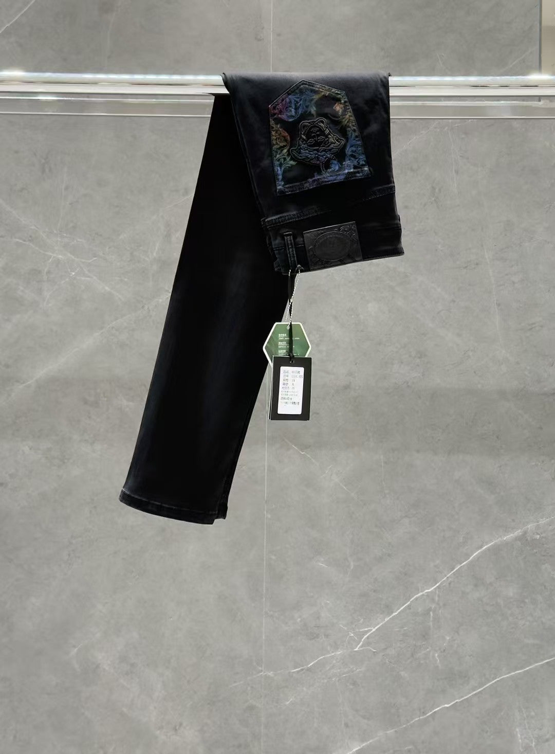 Dark denim jeans with a folded hem and colorful graphic patch on the back pocket area.