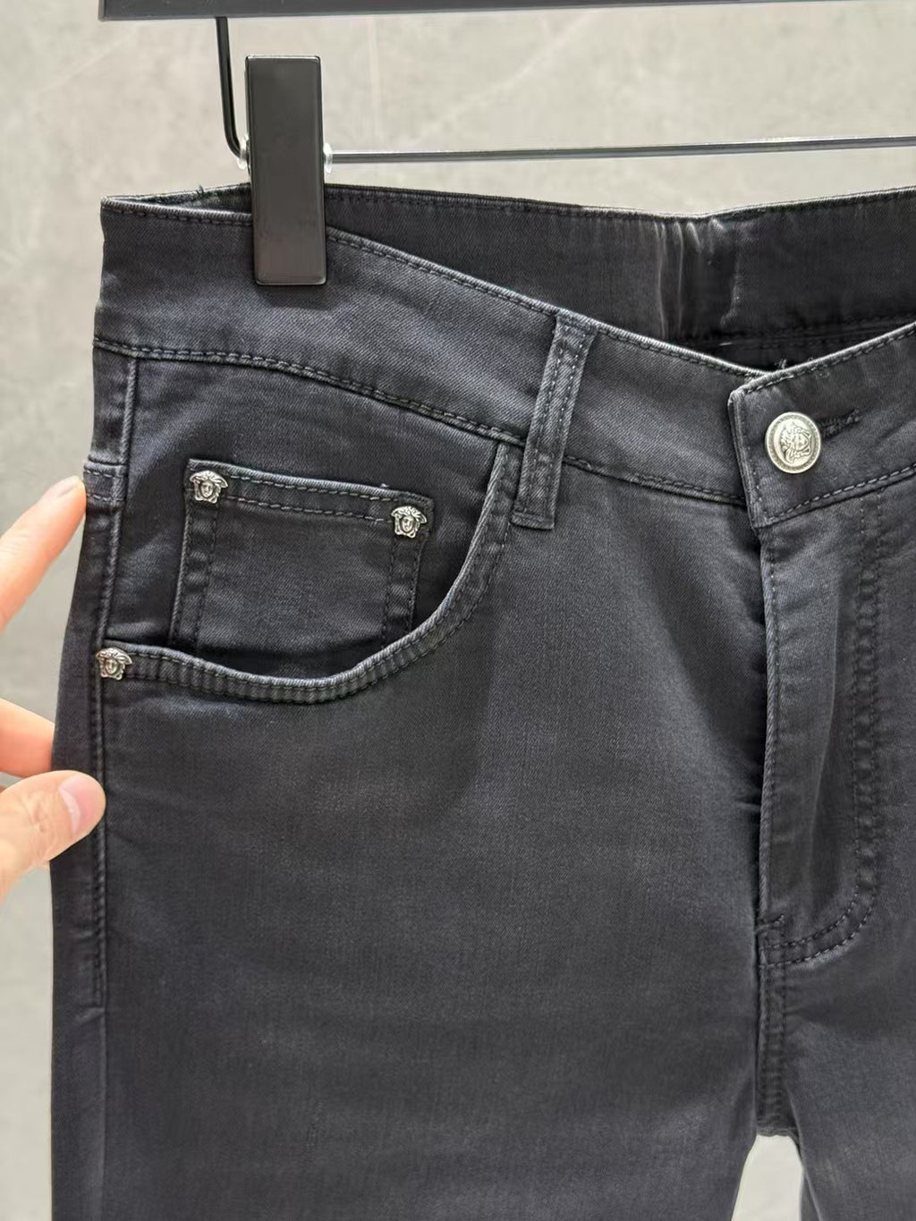 Dark denim jeans close-up of front pockets with metal buttons and stitched detailing.