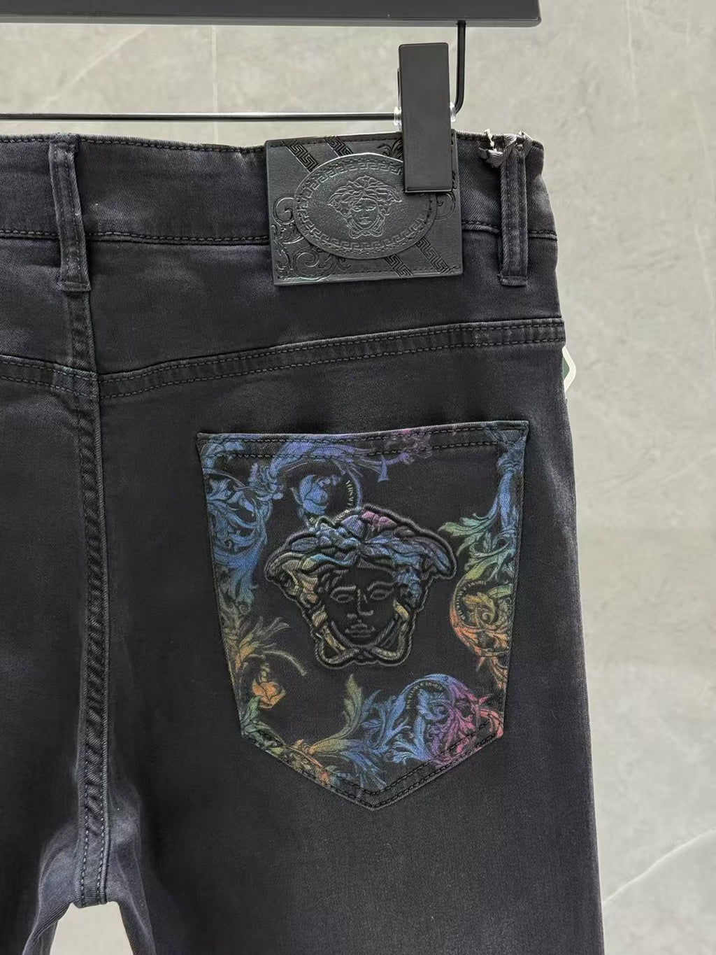 Dark denim jeans close-up of waist tag and blue graphic patch on the front pocket.