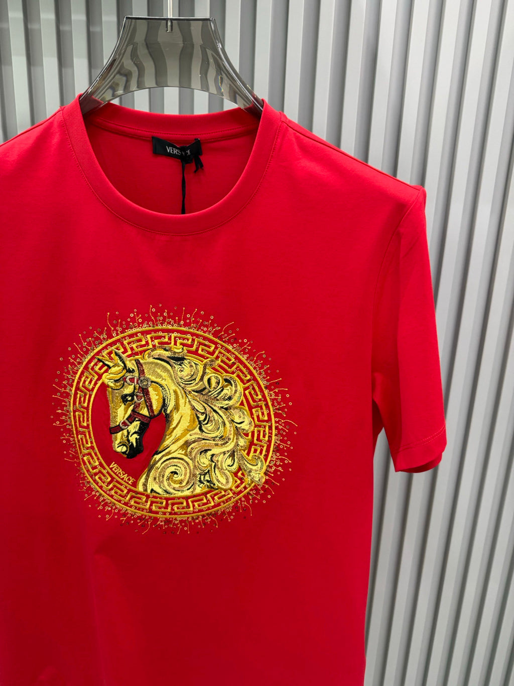 Versace red T-shirt close-up, gold lion medallion graphic, crew neck and short sleeves