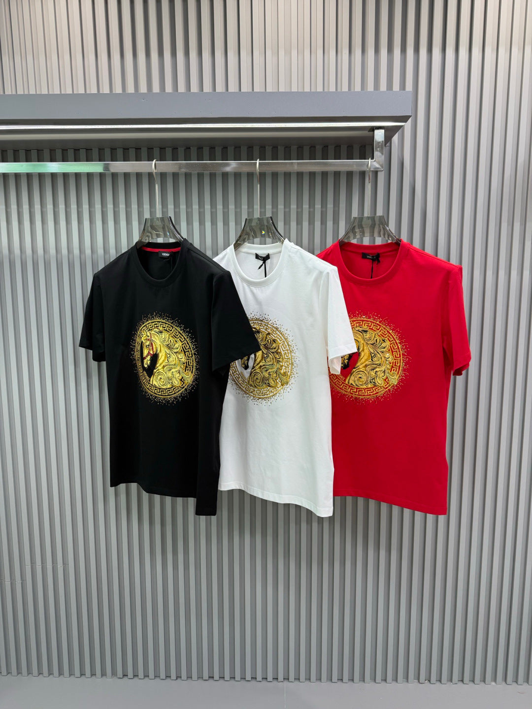 Three T-shirts: black, white, and red crew-necks with matching gold lion medallion prints