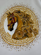 Close-up of gold horse crest emblem with Greek key border and rhinestone-like dots