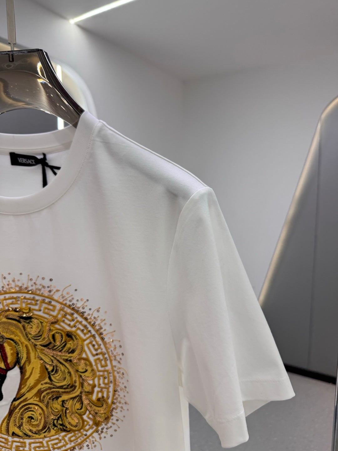White T-shirt showing shoulder and sleeve with part of gold horse emblem print