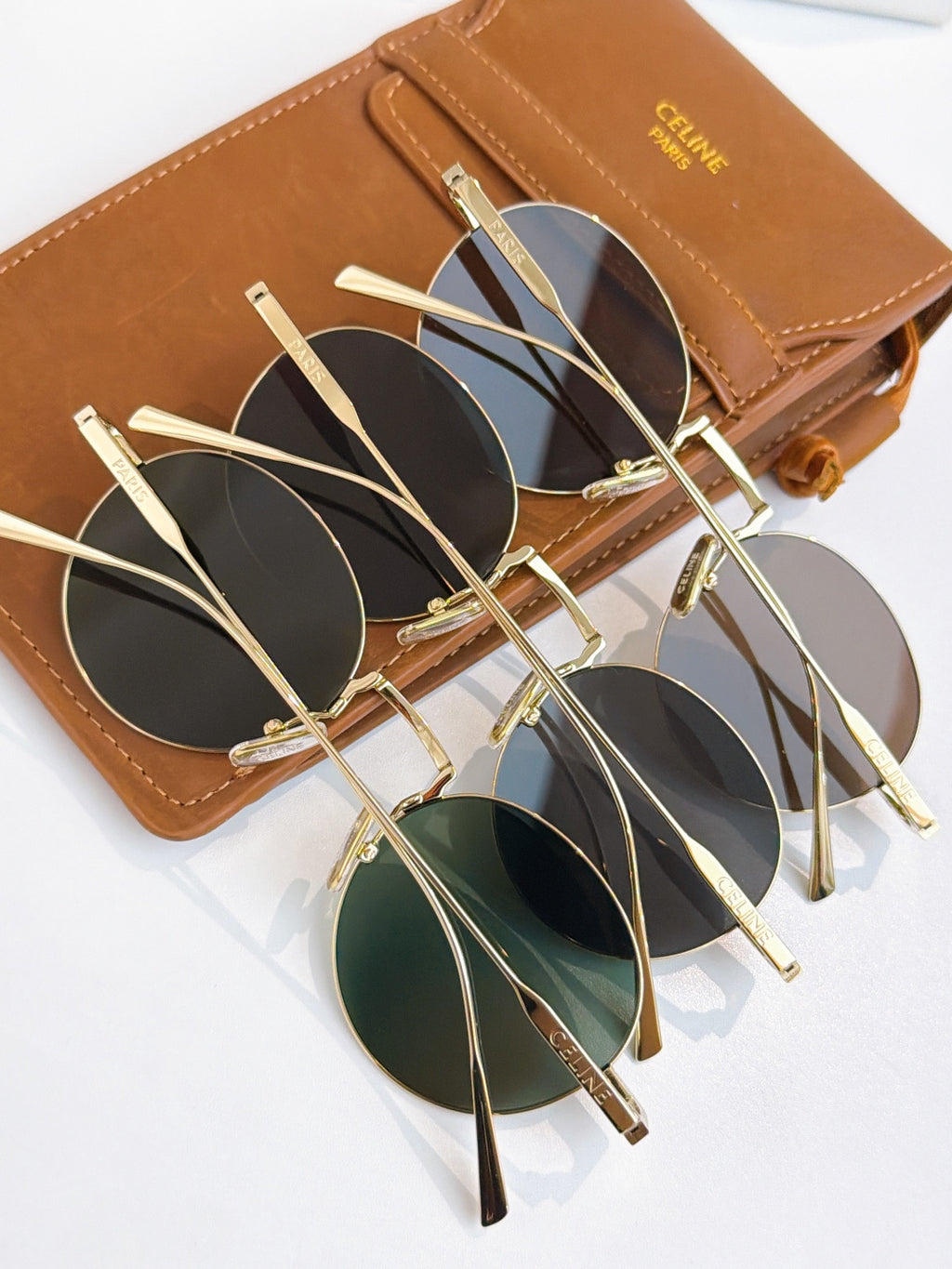 Multiple round gold-frame sunglasses with dark lenses stacked on a brown case.