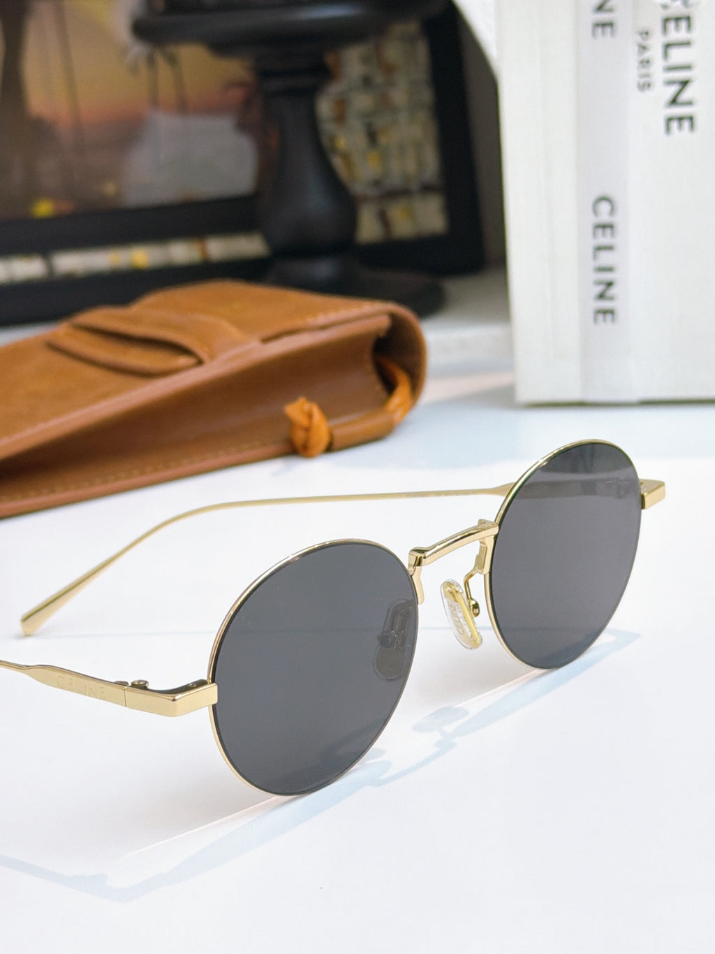 Round gold-frame sunglasses with dark gray lenses laid on a white surface.