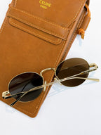 Round gold-frame sunglasses with dark lenses on top of a brown glasses case.