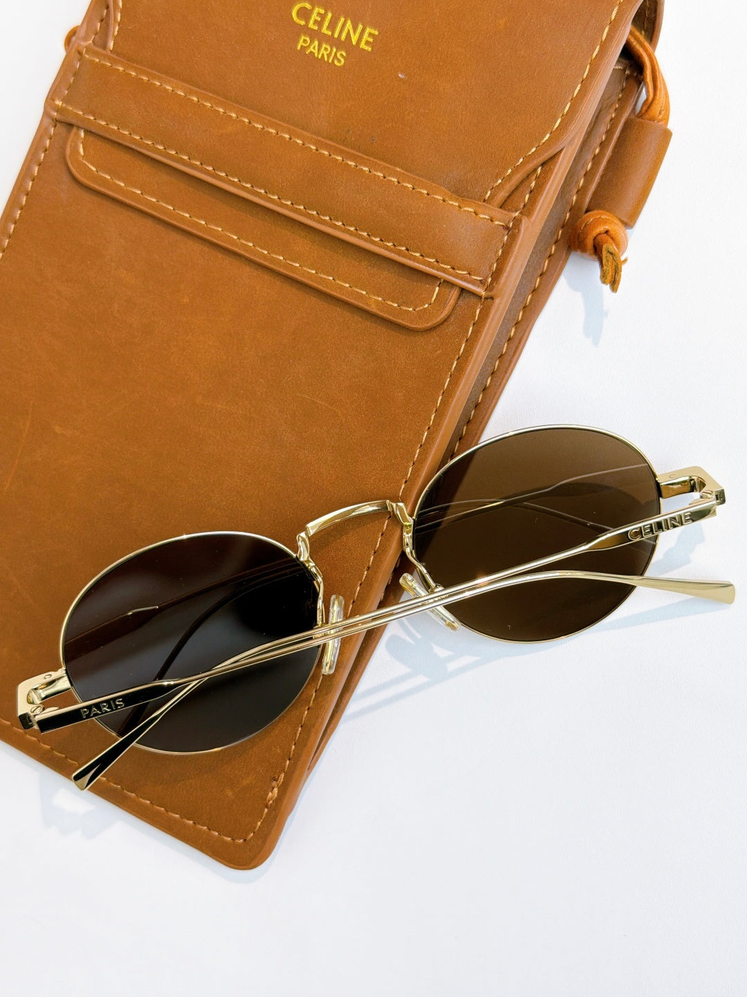 Round gold-frame sunglasses with dark lenses on top of a brown glasses case.