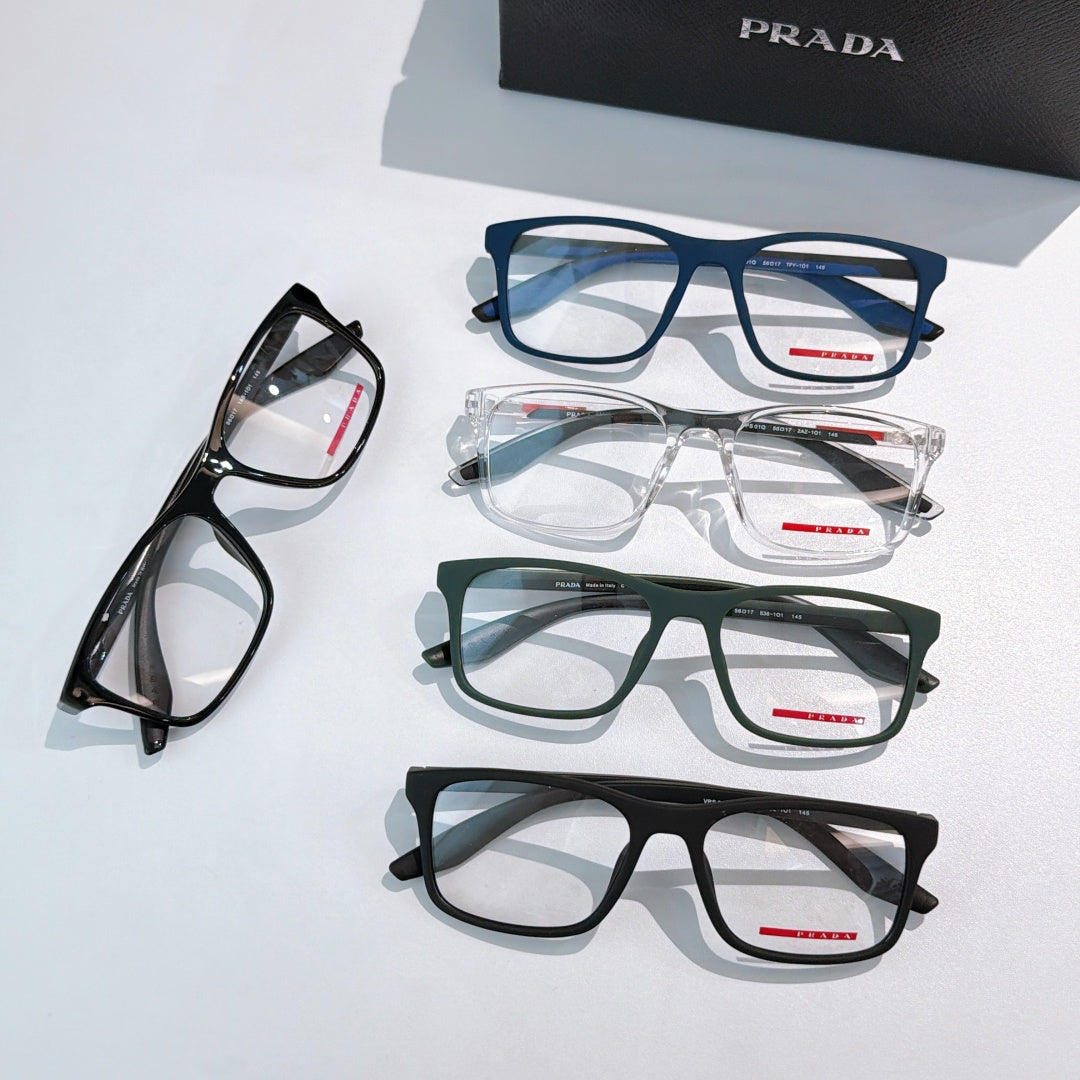 Prada glasses laid out: blue, clear, green, and black frames with red PRADA logos