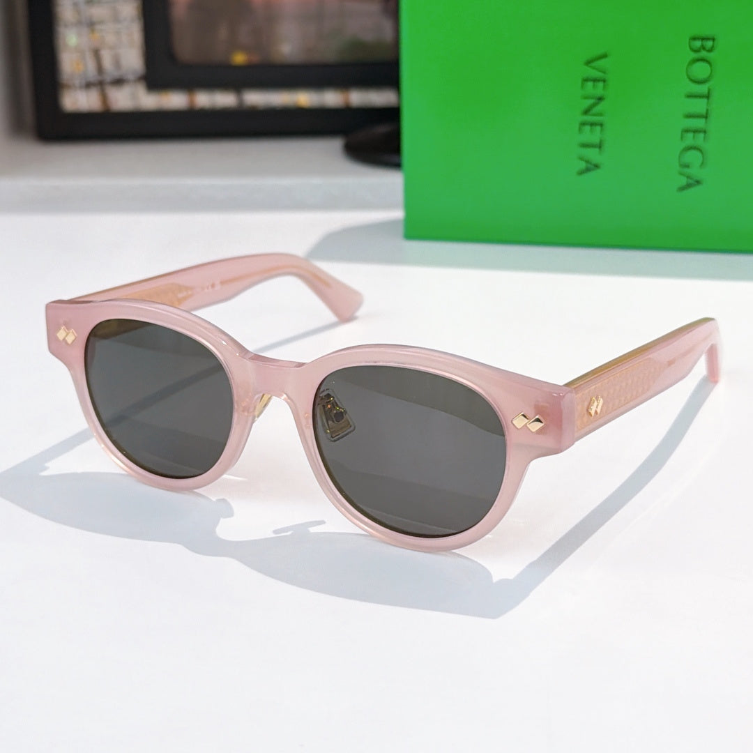 Sunglasses with pink frame, dark lenses, and gold-patterned temples