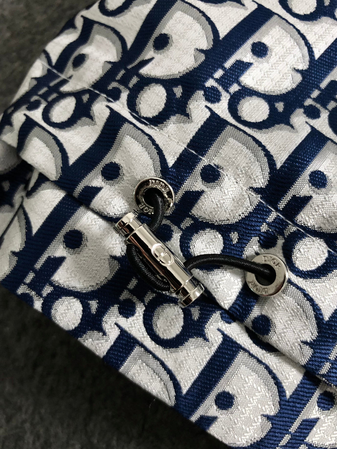 Close-up of jacket metal zipper slider and pull tab on Dior monogram fabric.