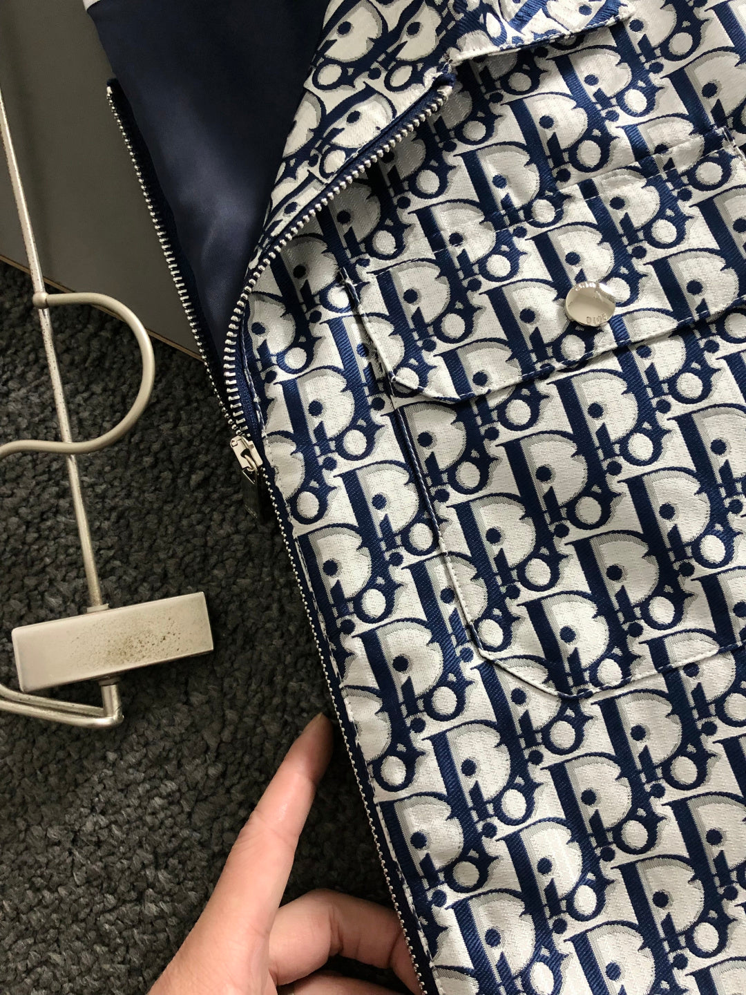 Close-up of Dior monogram jacket zipper and navy-and-white patterned fabric.