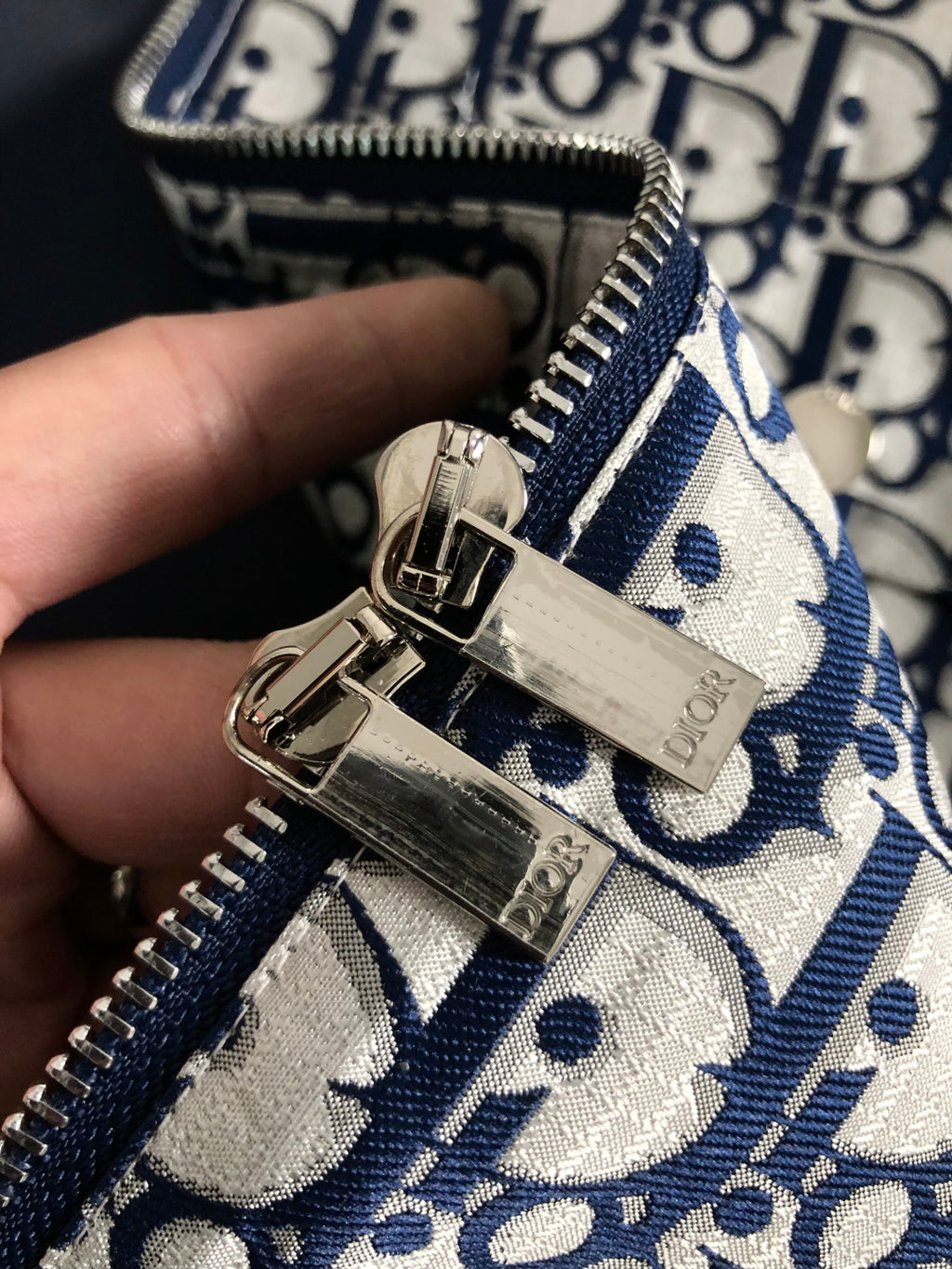 Close-up of jacket zipper pull and metal hardware on Dior monogram fabric.