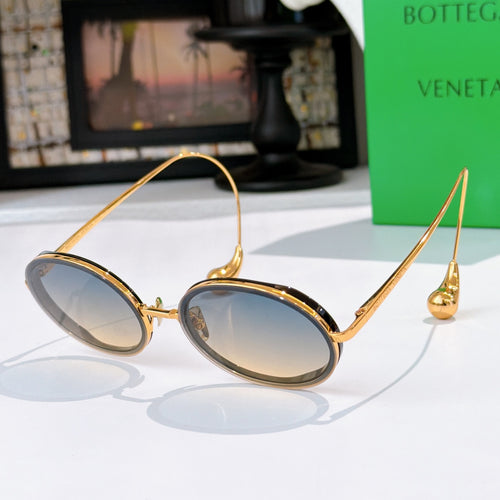 Oval sunglasses with blue-gray tinted lenses and gold-tone metal frames.