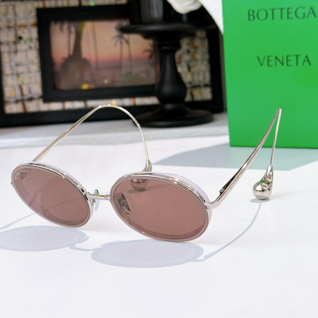 Oval sunglasses with light mauve tinted lenses and clear-toned frame with silver hardware.