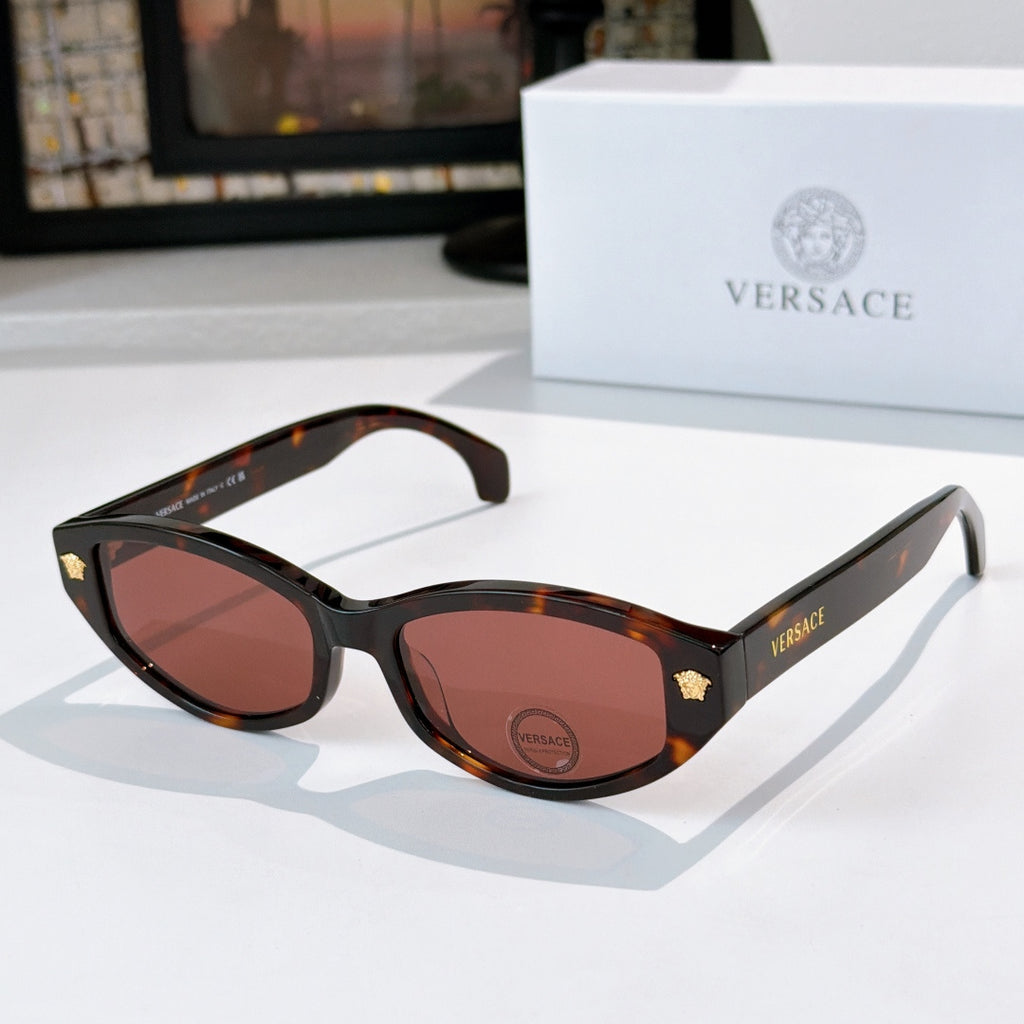 Black cat-eye sunglasses with dark brown lenses and gold emblem temple details