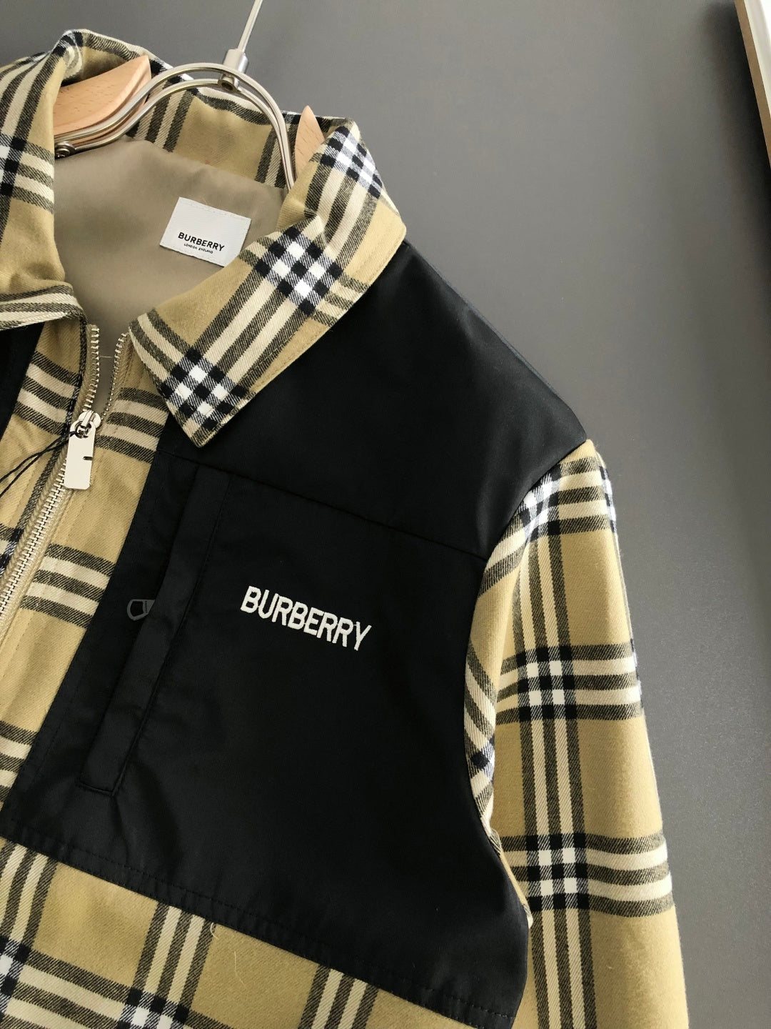 Detail view of plaid-collar jacket with black front panel and “BURBERRY” logo patch.