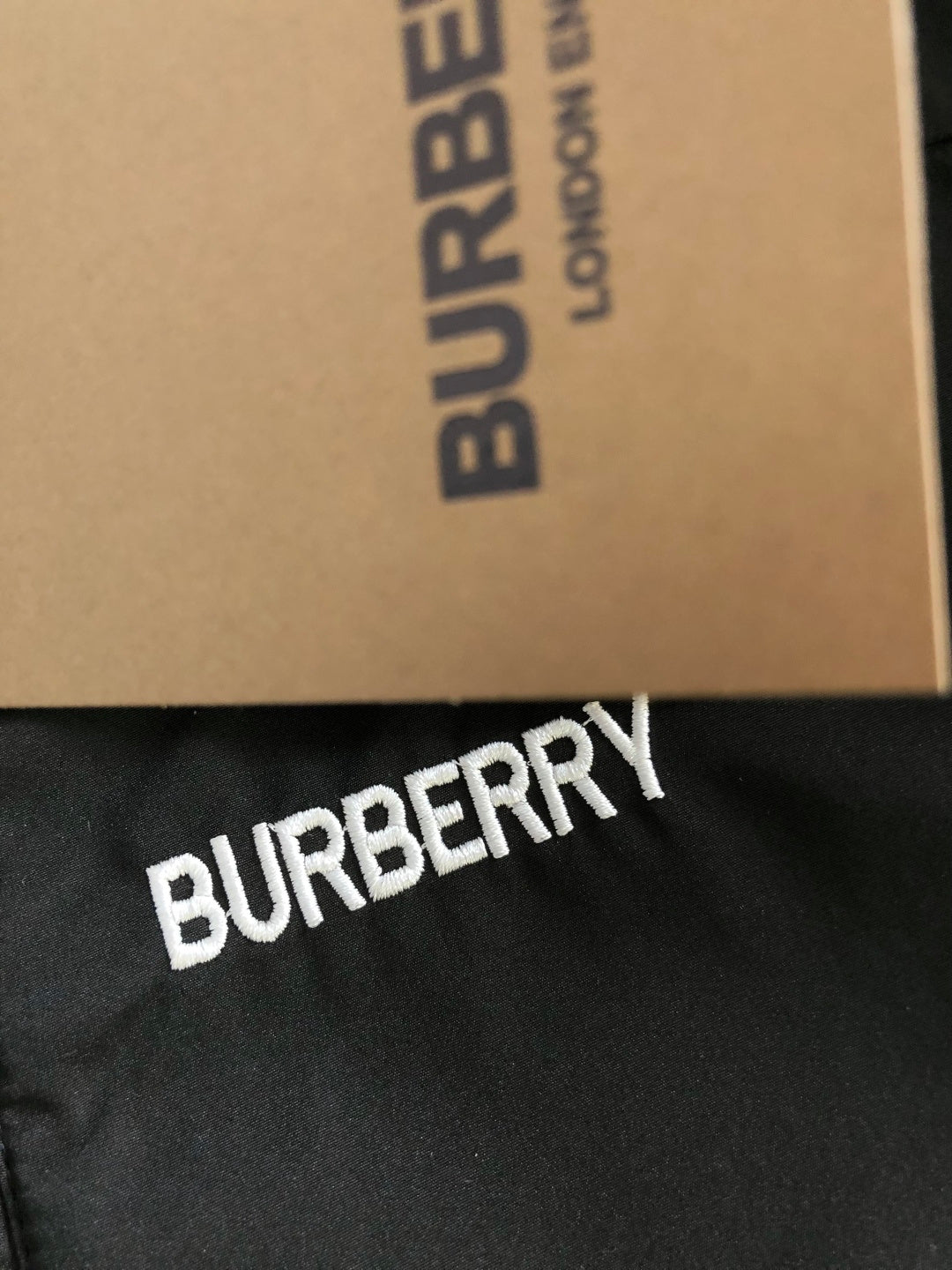 “BURBERRY” logo print on black fabric of a plaid collar jacket.