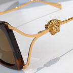 Close-up of oversized sunglasses temple with gold lion emblem and gold-toned arms.