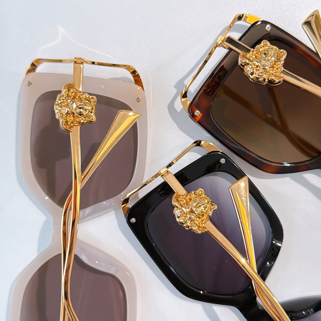 Pair of square sunglasses with gold accents, gold lion emblems, translucent and dark lenses.