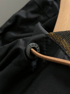 Black jacket fabric close-up with round metal snap and tan pull cord