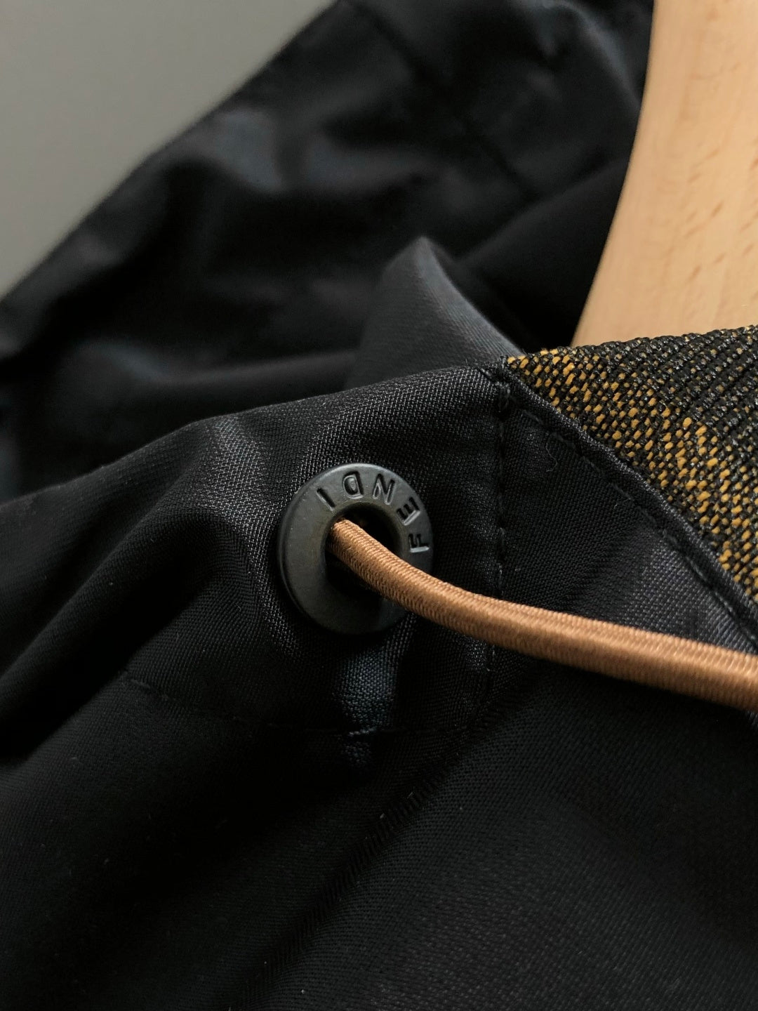 Black jacket fabric close-up with round metal snap and tan pull cord