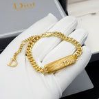 Dior gold-tone chain bracelet with textured bar charm held in white gloves.