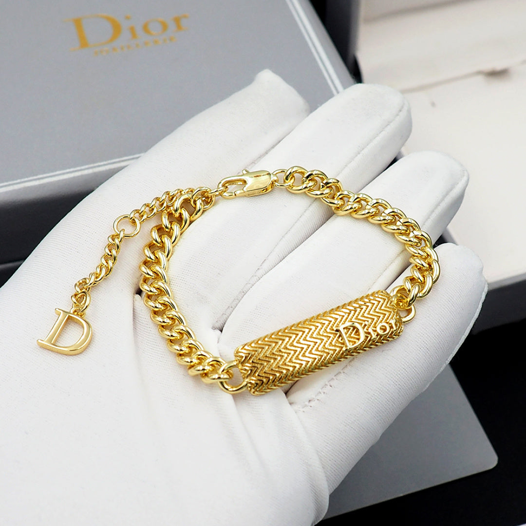 Dior gold-tone chain bracelet with textured bar charm held in white gloves.