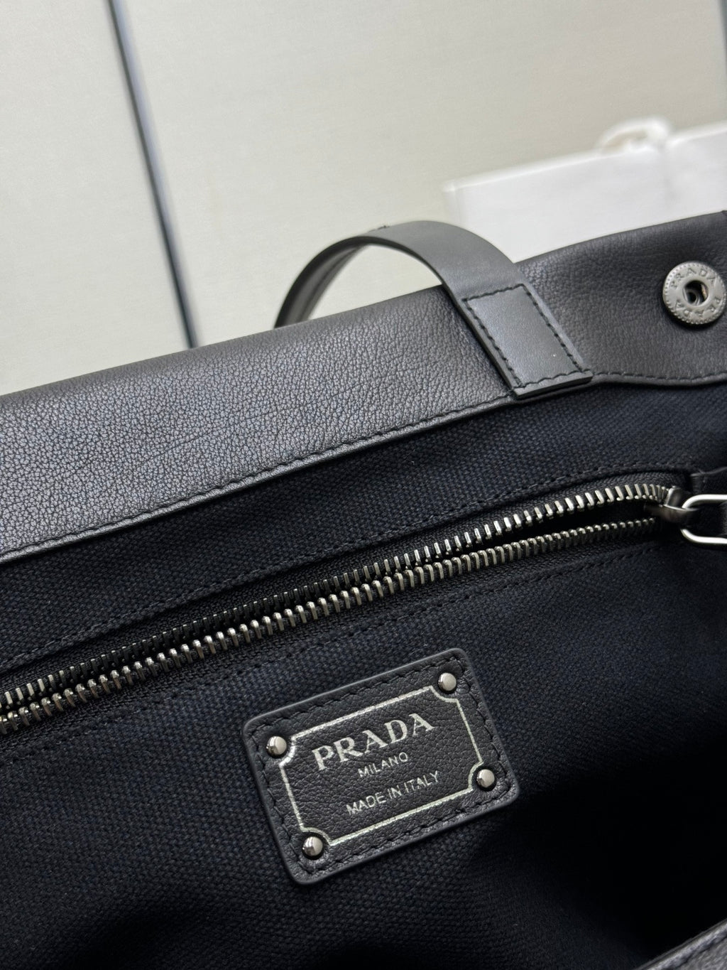 Prada Milano leather patch label on black bag beside zipper hardware