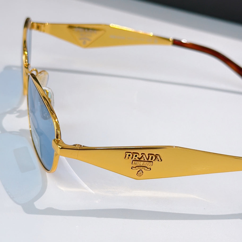Prada sunglasses close-up, gold frame and logo temple, blue-tinted lenses