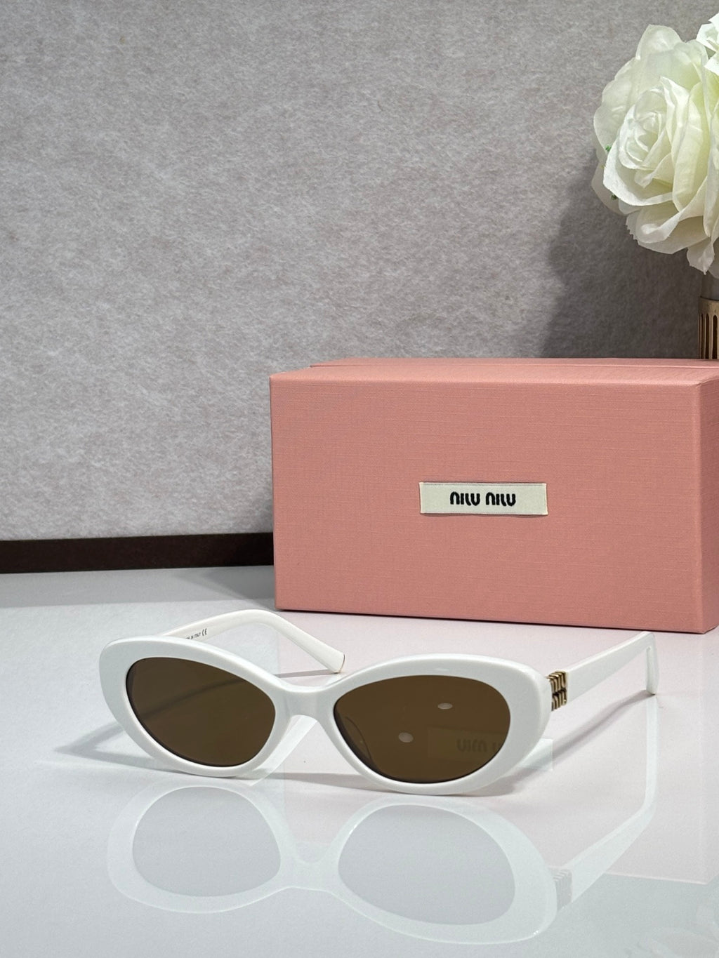 MiuMiu cat-eye sunglasses with white frames and dark oval lenses, gold-tone hinges