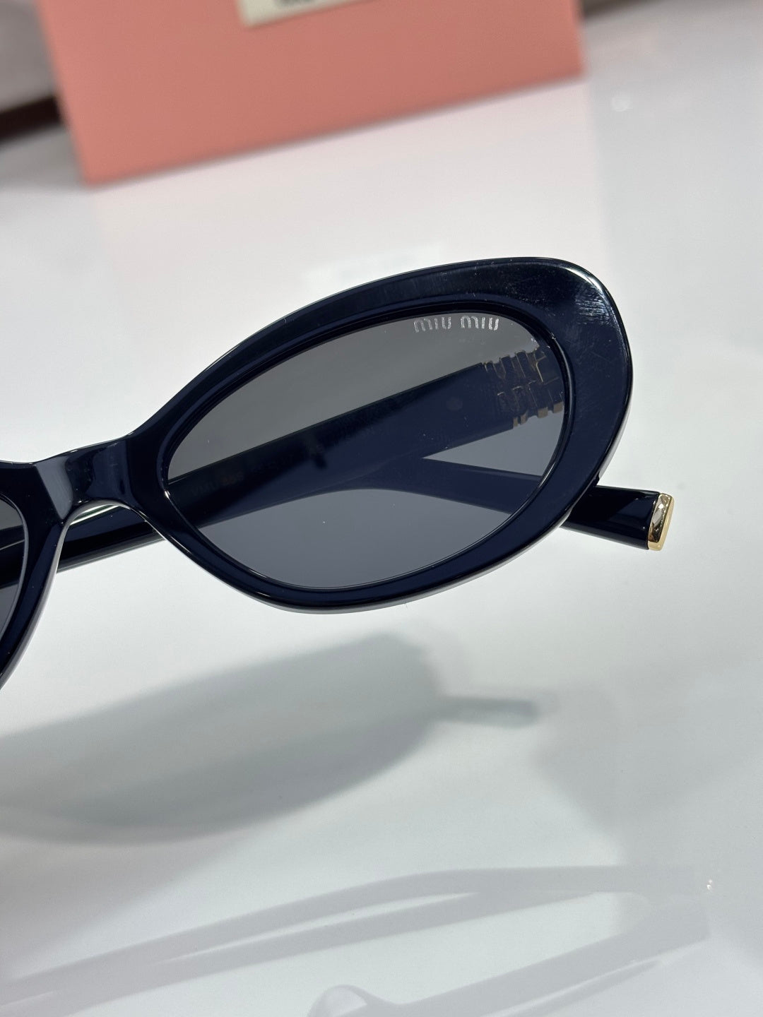 MiuMiu cat-eye sunglasses lens close-up with dark frame and gold-tone hinge