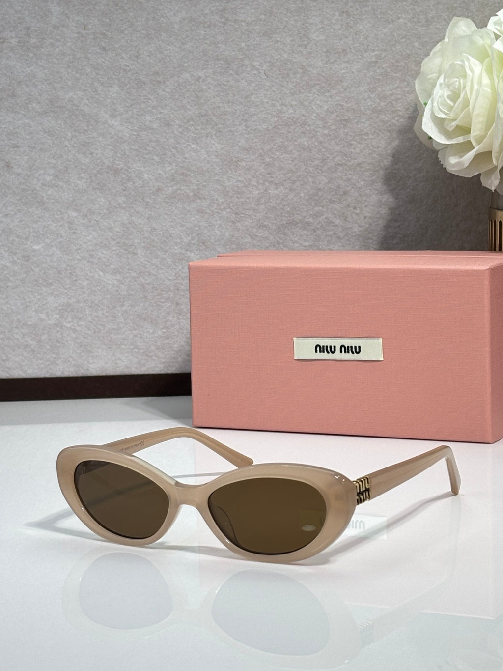 MiuMiu cat-eye sunglasses with beige frames and dark oval lenses, gold-tone details