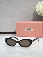 MiuMiu cat-eye sunglasses with dark frames, oval lenses, and gold-tone accents