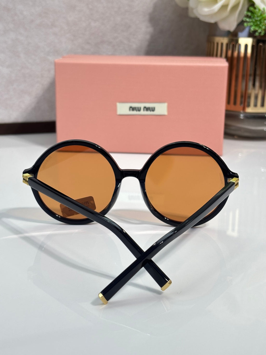 MiuMiu sunglasses with black round frames and amber tinted lenses, logo on lens