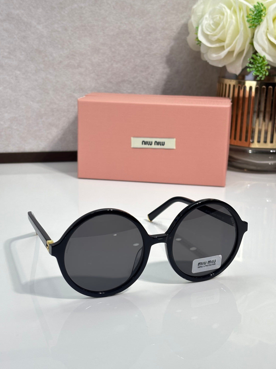 MiuMiu sunglasses with black round frames and dark lenses, metal logo on lens