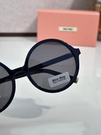 MiuMiu sunglasses close-up of black round frame and dark lens with logo