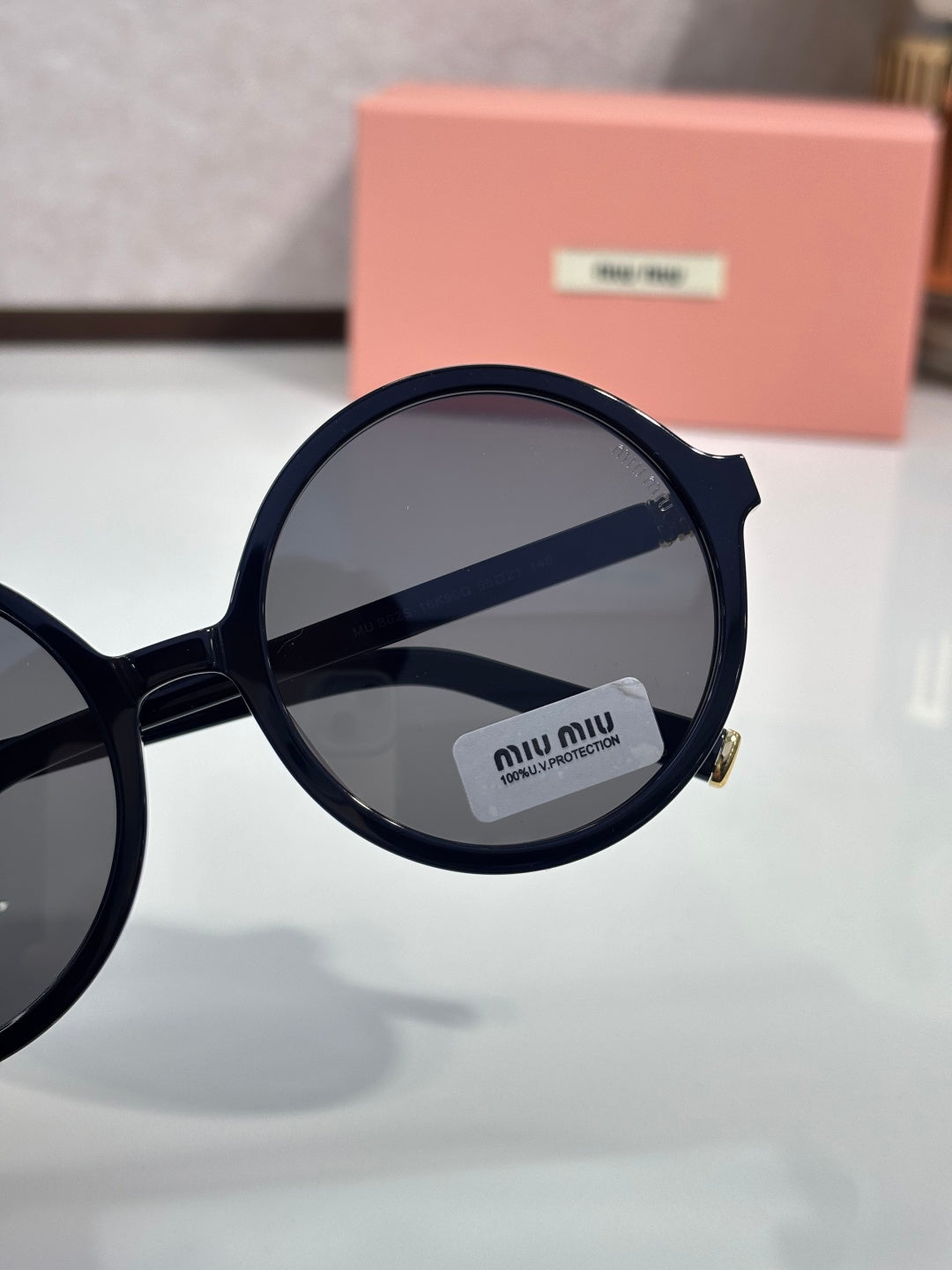 MiuMiu sunglasses close-up of black round frame and dark lens with logo