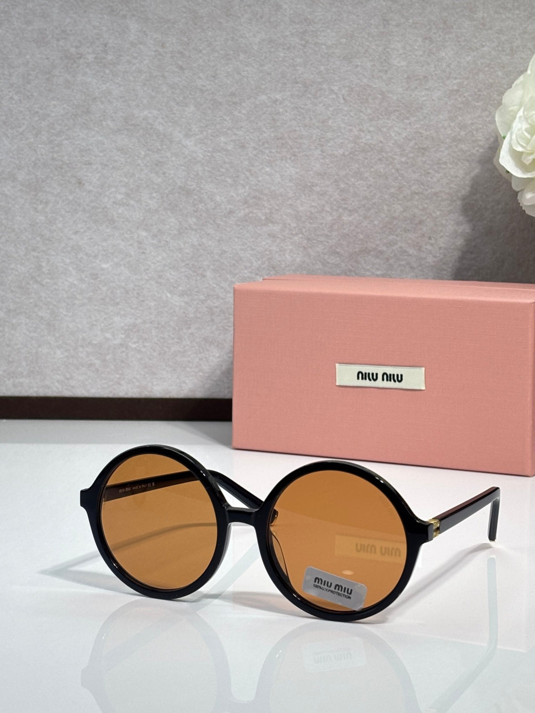 MiuMiu sunglasses with black round frames and amber tinted lenses, logo on lens