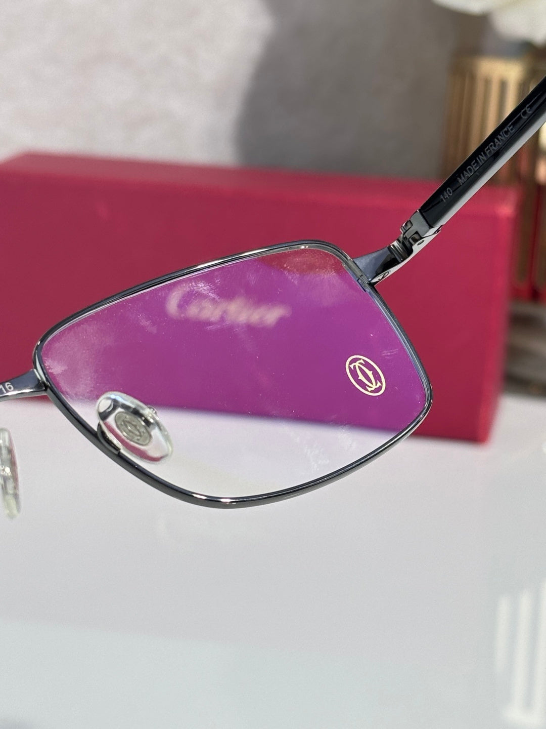Black eyeglasses frame with purple-tinted lens and metal temple logo