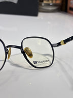 Close-up of black round eyeglass frame with gold temple and inner lens mark.