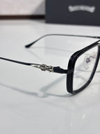 Close-up of black eyeglass temple with ornate metal detail and clear lens.