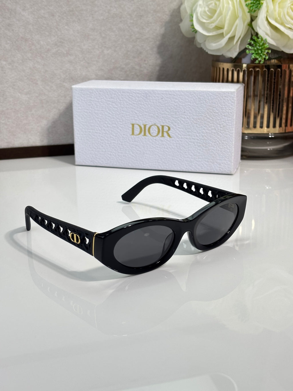 Dior sunglasses with black oval frames and dark lenses, gold accents