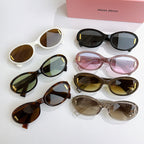 Assorted oval sunglasses with gold logo temples in white, black, pink, tortoise, and clear