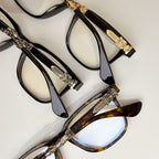 Assorted eyeglass frames stacked: black and tortoise with gold temple accents