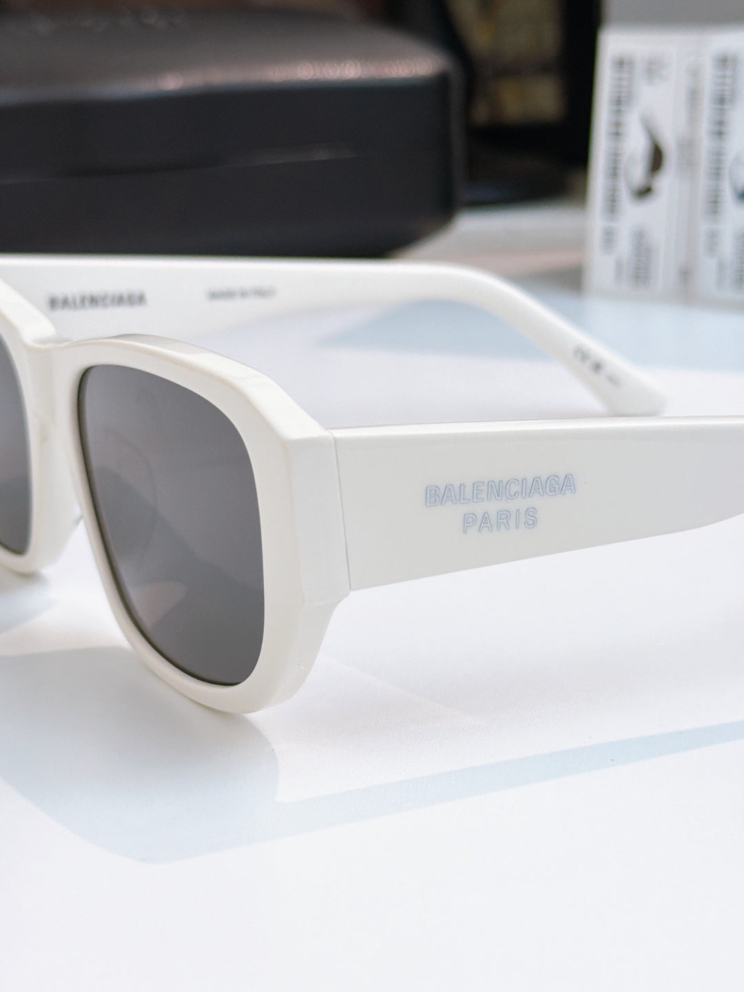 Balenciaga white sunglasses close-up with dark lenses and engraved side text