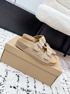 Beige Louis Vuitton slide sandals on box, showing side straps with adjustable buckles.
