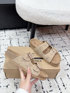 Beige Louis Vuitton slide sandals with two buckle straps, held above the box.