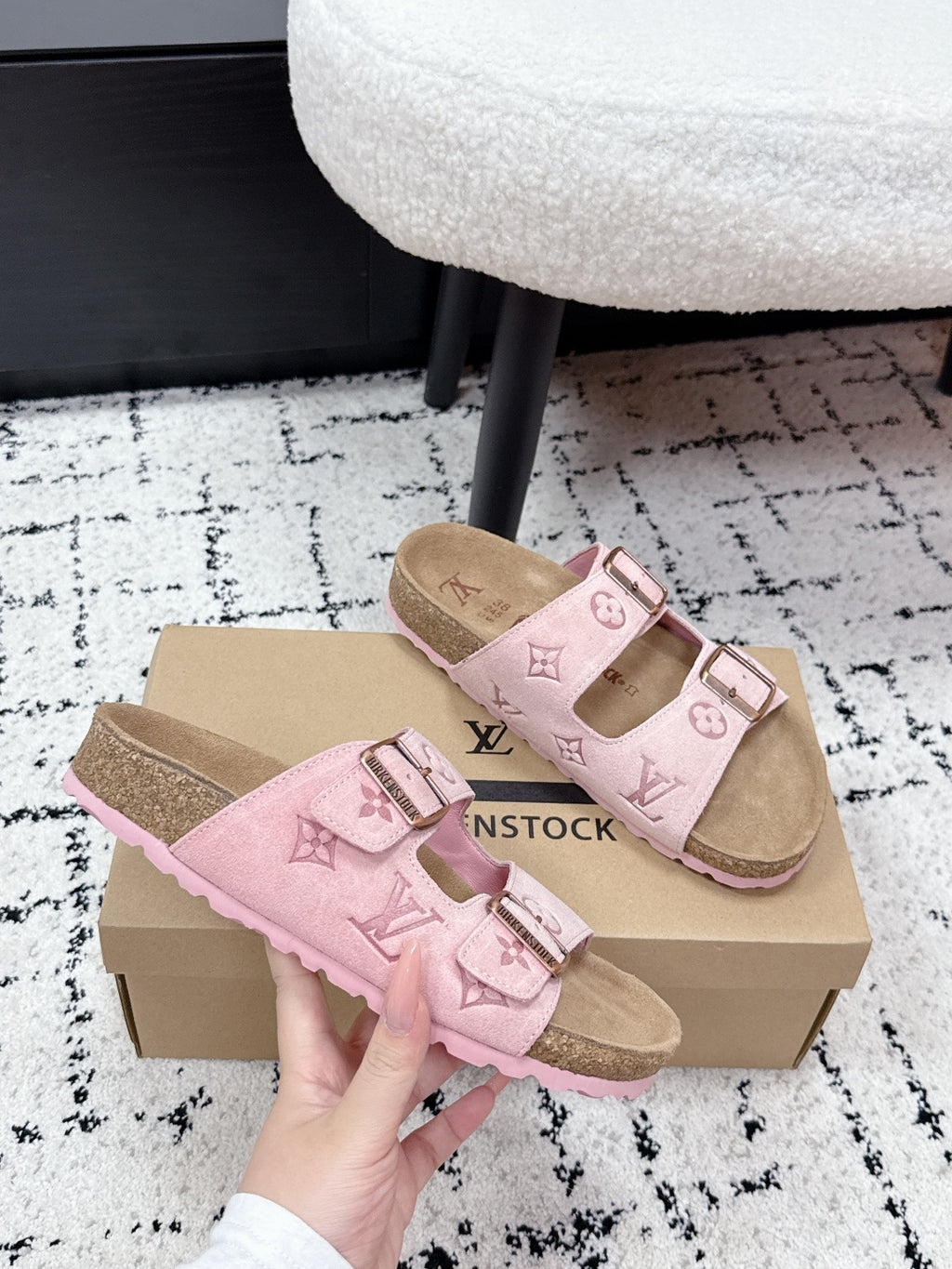 Louis Vuitton pink slide sandals with two buckled straps, held in front of the box