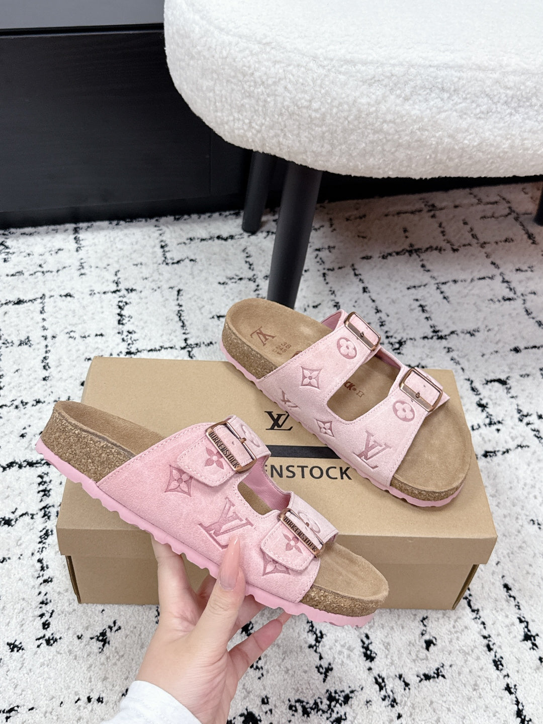 Louis Vuitton pink slide sandals with two buckled straps, held in front of the box